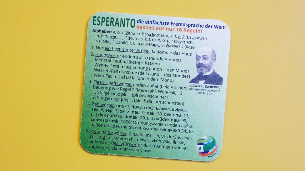 Ein Bierdeckel mit den 16 Regeln auf den die Fremdsprache Esperanto basiert. Fotografiert vor einem gelben Hintergrund.