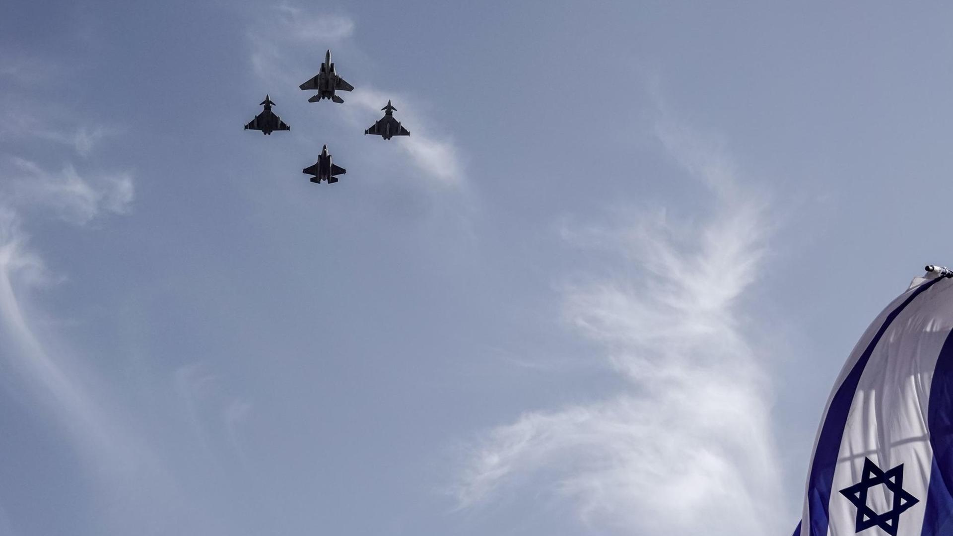 Die Flagge Israels weht im Wind, während am Himmel vier Kampfjets fliegen. Die Flagge Israels weht im Wind, während am Himmel vier Kampfjets fliegen.