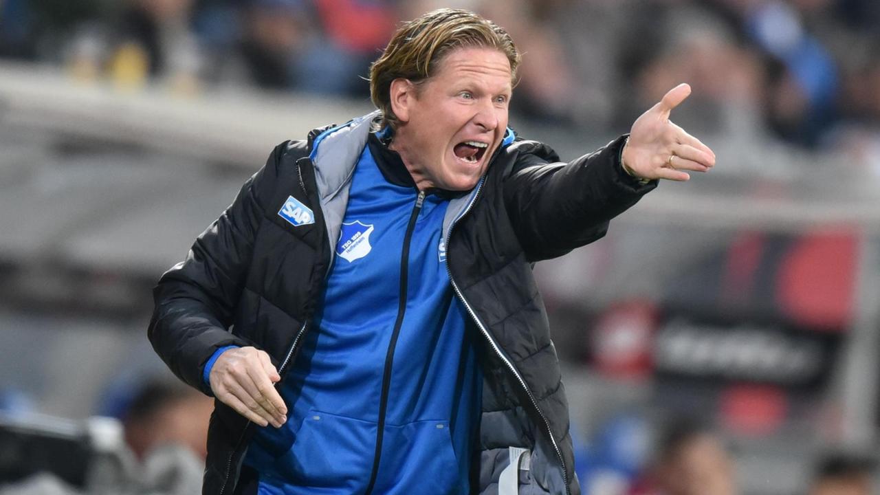 Markus Gisdol hat eine blaue Trainingsjacke und eine schwarze Winterjacke an.