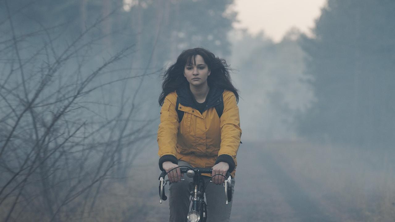 Lisa Vicari in der Rolle der Martha Nielsen, fährt in einer gelben Jacke Fahrrad durch den Wald.