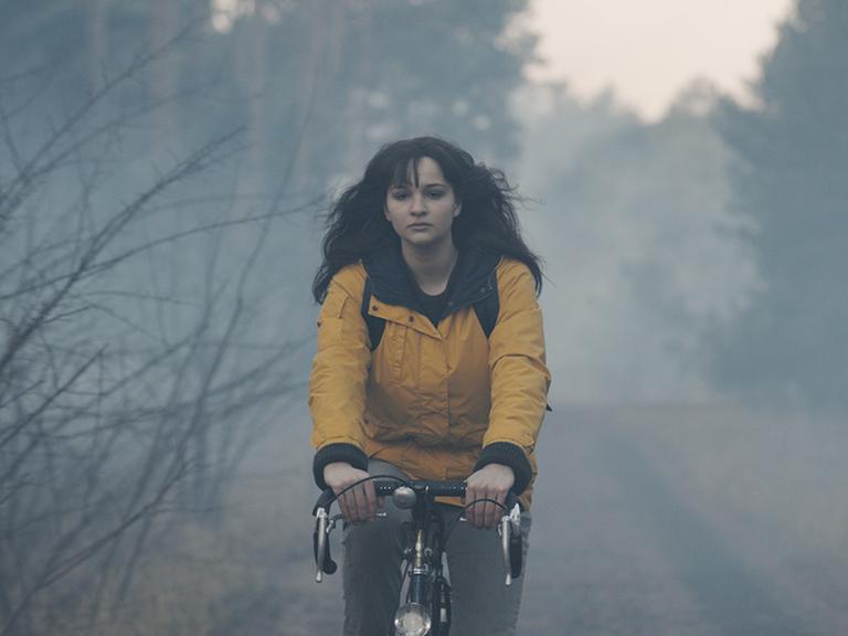Lisa Vicari in der Rolle der Martha Nielsen, fährt in einer gelben Jacke Fahrrad durch den Wald.