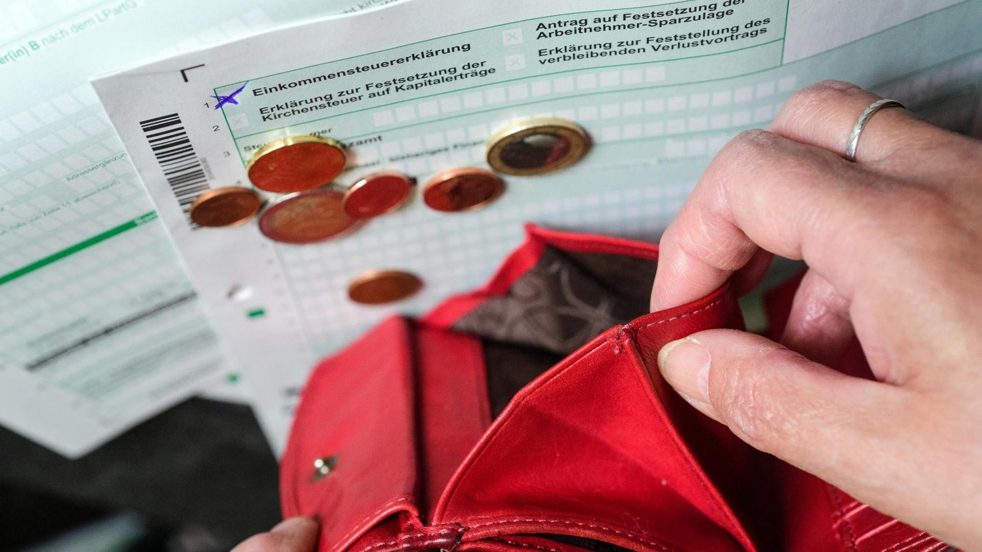 Eine Frau entleert die letzten Münzen aus ihrer Geldbörse auf ein Steuerformular, das am 12.04.2017 in Berlin auf dem Tisch liegt.