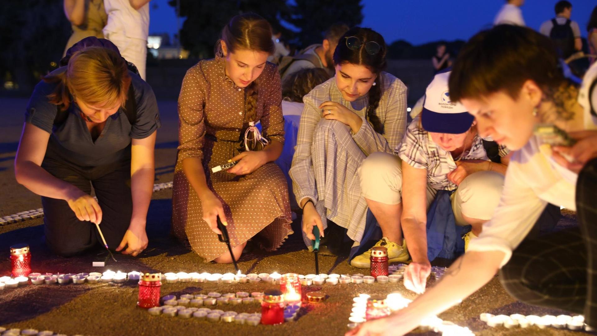 Junge Frauen knien auf dem Marsfeld in St. Petersburg und zünden Kerzen zum Gedenken an den Überfall der Deutschen auf die Sowjetunion 1941 an.