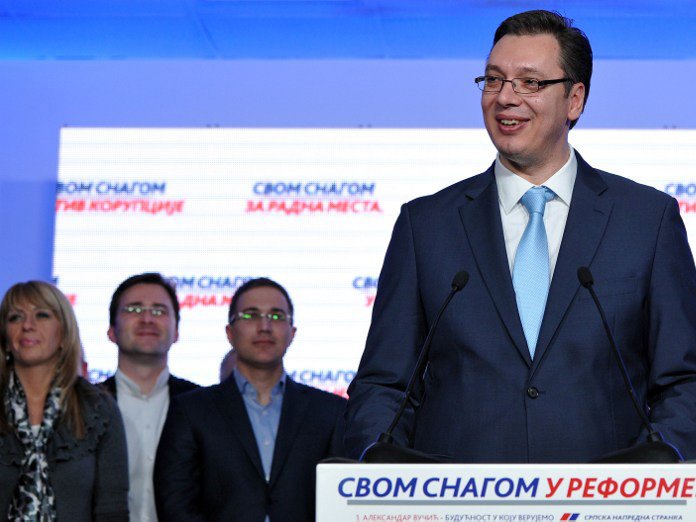 Aleksandar Vucic auf einer Pressekonferenz nach seinem Wahlsieg an einem Rednerpult, links von ihm drei Parteianhänger