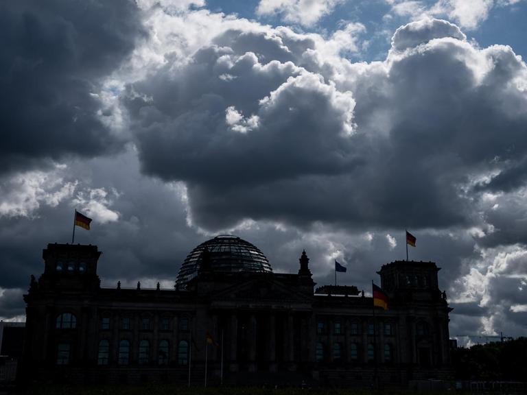 Die Sonne versteckt sich hinter dunklen Wolken über dem Reichstag, dem Sitz des Deutschen Bundestags.