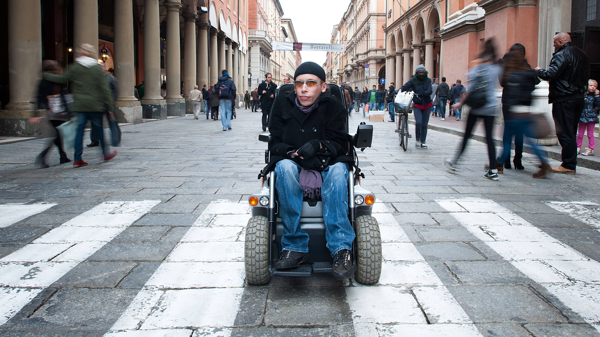 Der an Muskeldystrophie erkrankte Maximiliano Ulivieri in Bologna. Ulivieri sitzt im Rollstuhl in einer Fußgängerstraße.
