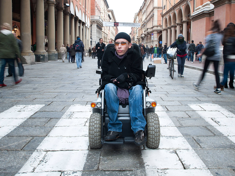 Der an Muskeldystrophie erkrankte Maximiliano Ulivieri in Bologna. Ulivieri sitzt im Rollstuhl in einer Fußgängerstraße.