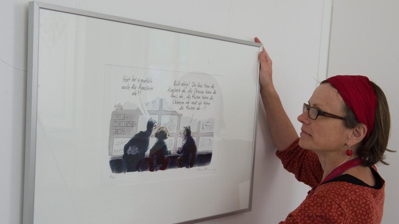 Franziska Pucher, Mitarbeiterin der Staatlichen Bücher- und Kupferstichsammlung, hängt am 02.06.2015 in der Ausstellung «Alles unter Kontrolle - 8. Triennale der Karikatur» im Sommerpalais in Greiz (Thüringen) eine Karikatur von Klaus Stuttmann auf.