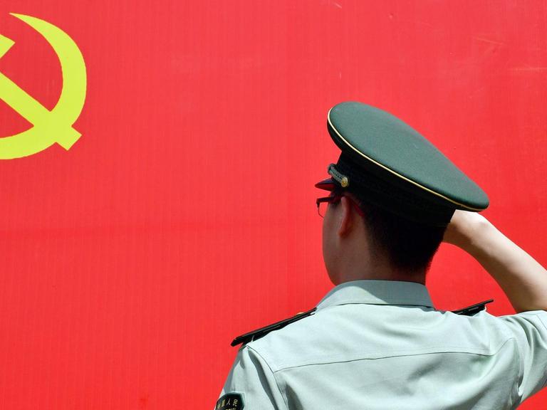 Ein Polizist salutiert vor der roten Flagge der Kommunistischen Partei Chinas.