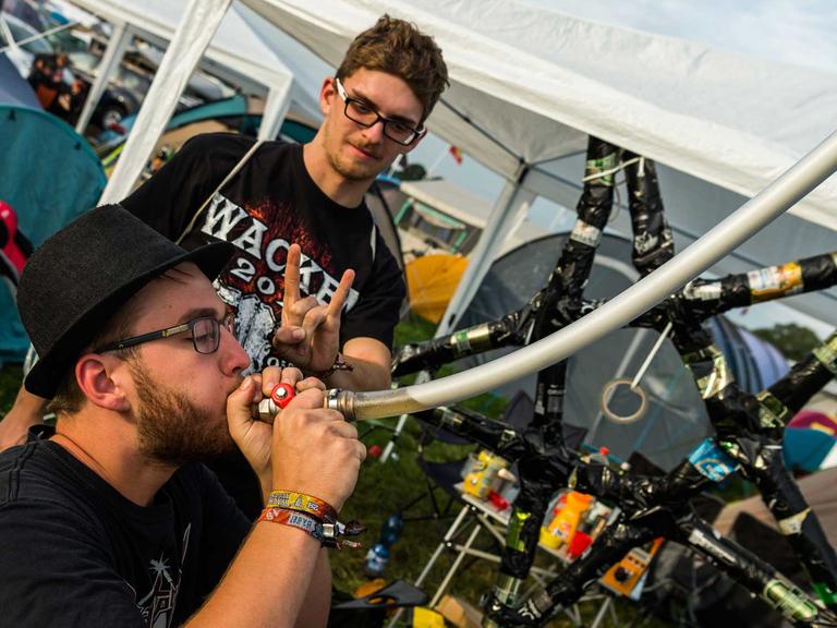 Peter aus Österreich trinkt am 02.08.2017 in Wacken (Schleswig-Holstein) auf dem Festivalgelände des Wacken Open Air im Camping Bereich einen halben Liter Bier aus einem Schlauch. Hinter ihm steht Marc und macht das Zeichen der Heavy-Metal-Fans, die "Pommesgabel". Das Wacken Open Air findet vom 03. bis 05.08.2017 statt.
