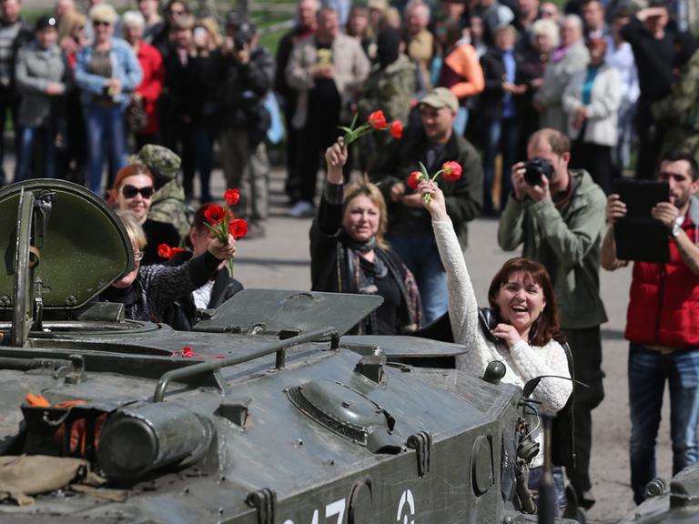 Frauen winken in der ukrainischen Stadt Slawjansk einem Panzer mit Blumen.