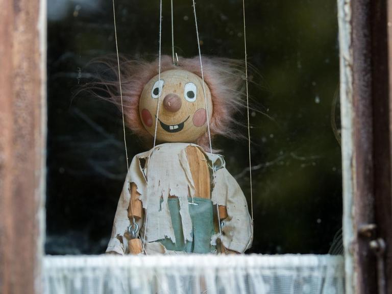 Marionette mit zerzaustem Haar und zerrissenen Klamotten in einem Fenster.