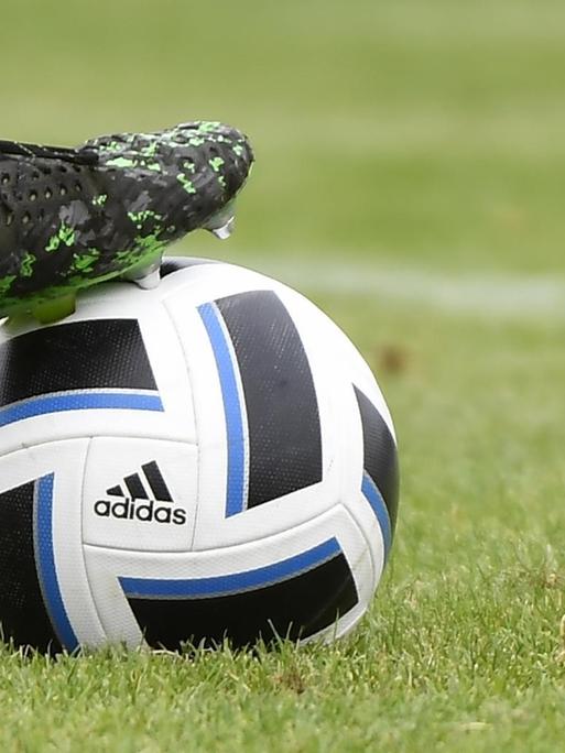 Symbolbild: Fussballschuh Puma auf einem Fussball von Adidas auf grünem Rasen.