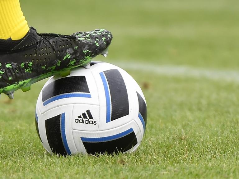 Symbolbild: Fussballschuh Puma auf einem Fussball von Adidas auf grünem Rasen.