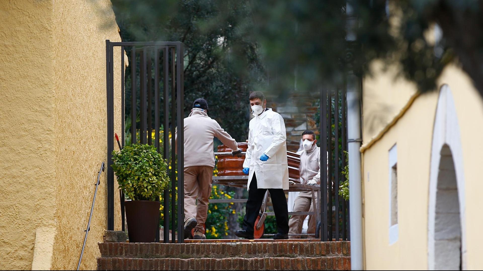 Bestatter in Schutzkleidung tragen aus einem Haus in Barcelona einen Sarg mit einem Menschen, der an Covid-19 gestorben ist.