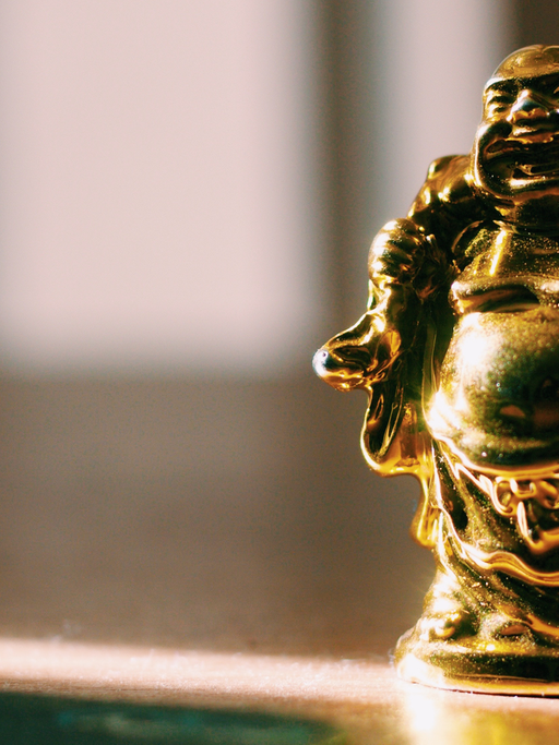 Eine kleine goldfarbene Statue eines lachenden Mönches wird von einem Sonnenstrahl angeleuchtet.