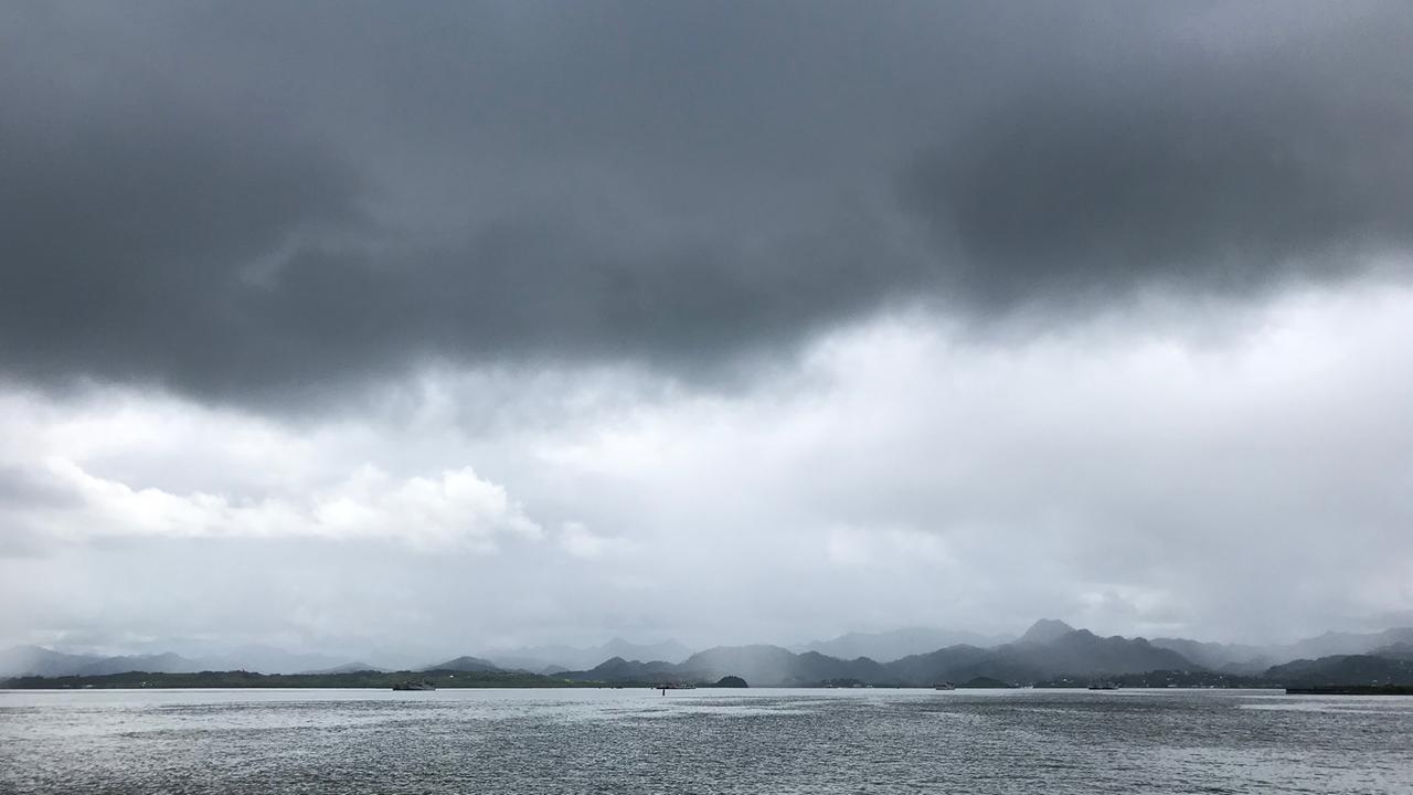 Vom Wasser aus ist eine Insel mit wolkenverhangenen Hügeln fotografiert.