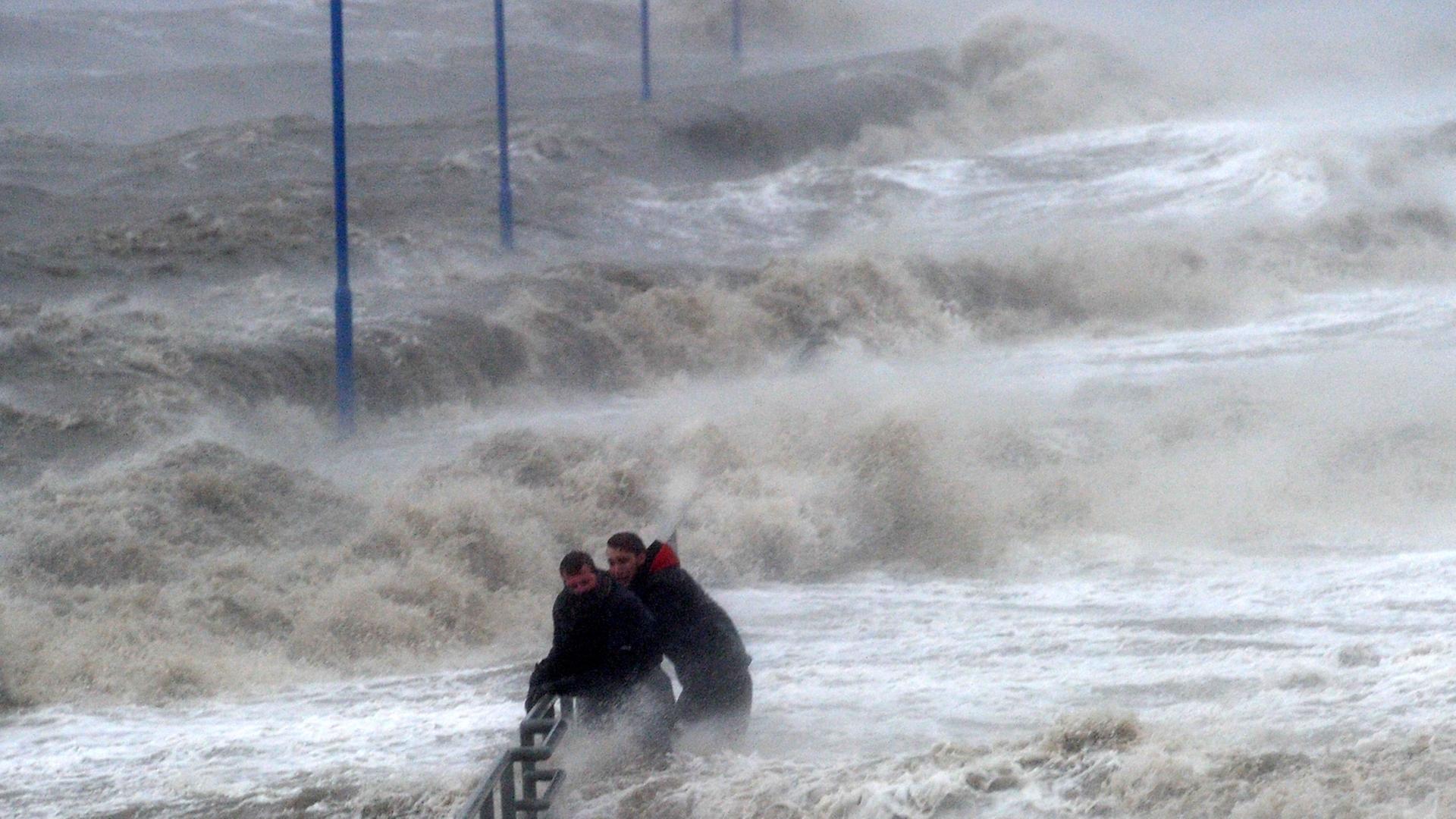 Zwei Männer halten sich an einem überfluteten Fähranleger am Geländer fest