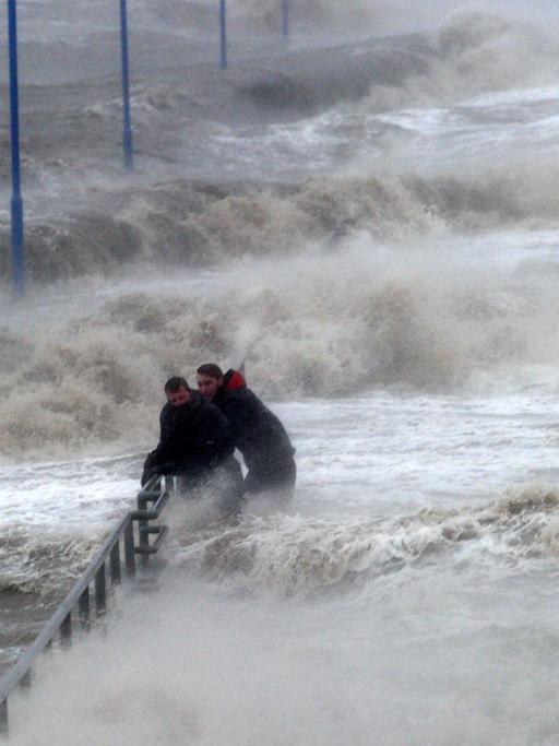 Zwei Männer halten sich an einem überfluteten Fähranleger am Geländer fest