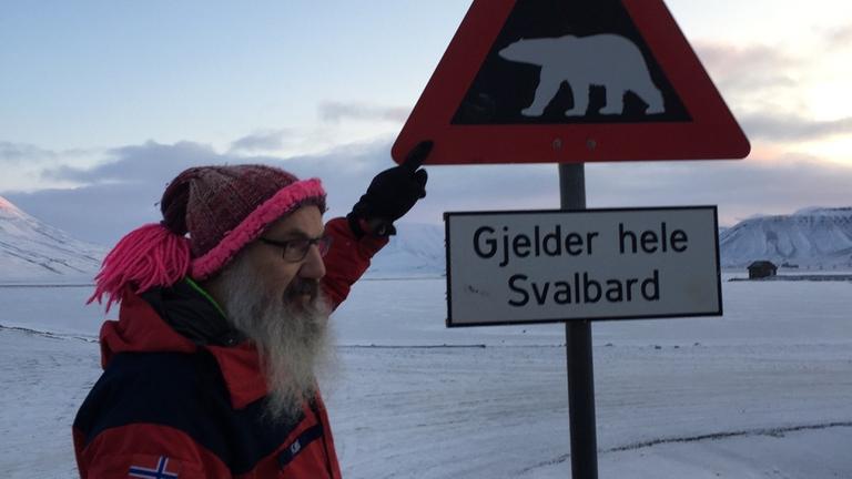 Polarforscher Kim Holmen vor einem Eisbär-Warnschild auf Spitzbergen