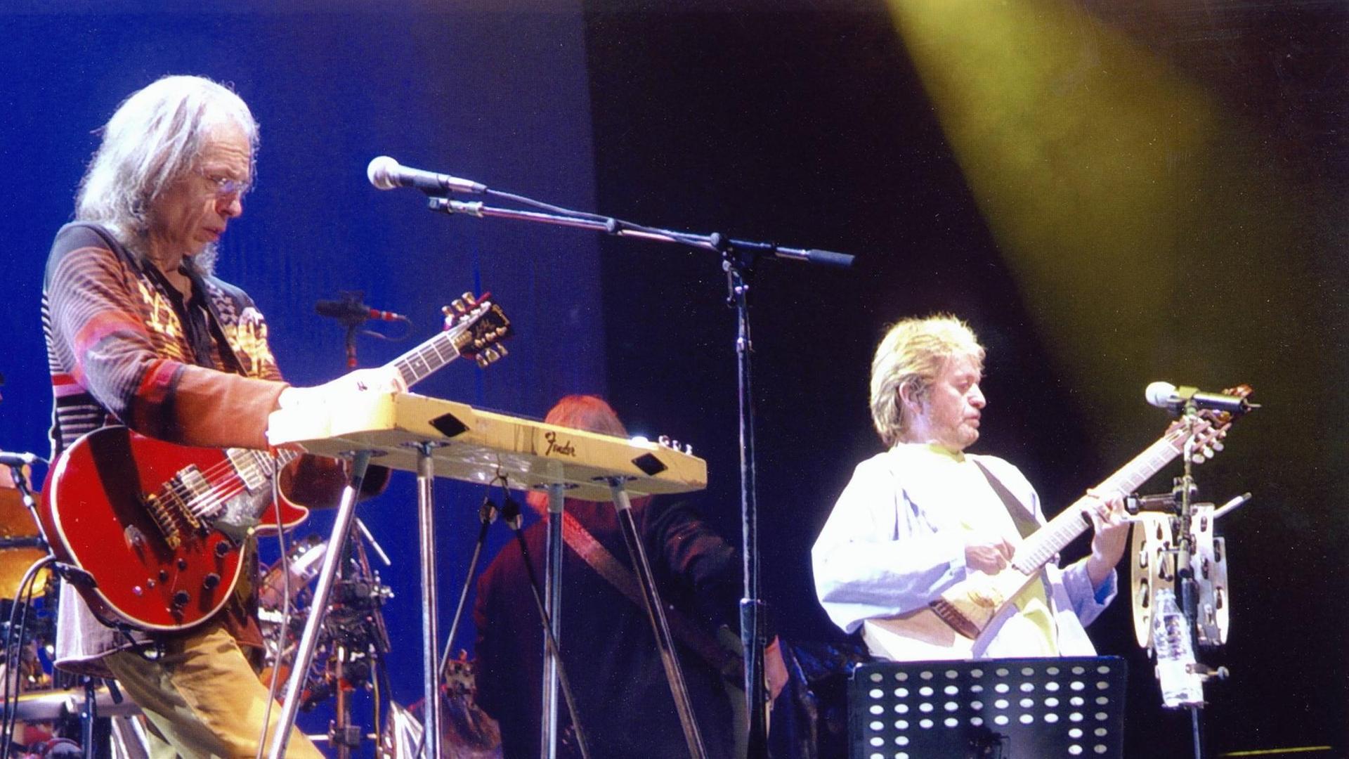 Zwei Männer stehen auf einer Bühne. Ein Mann spielt Gitarre, ein Mann spielt Bass.