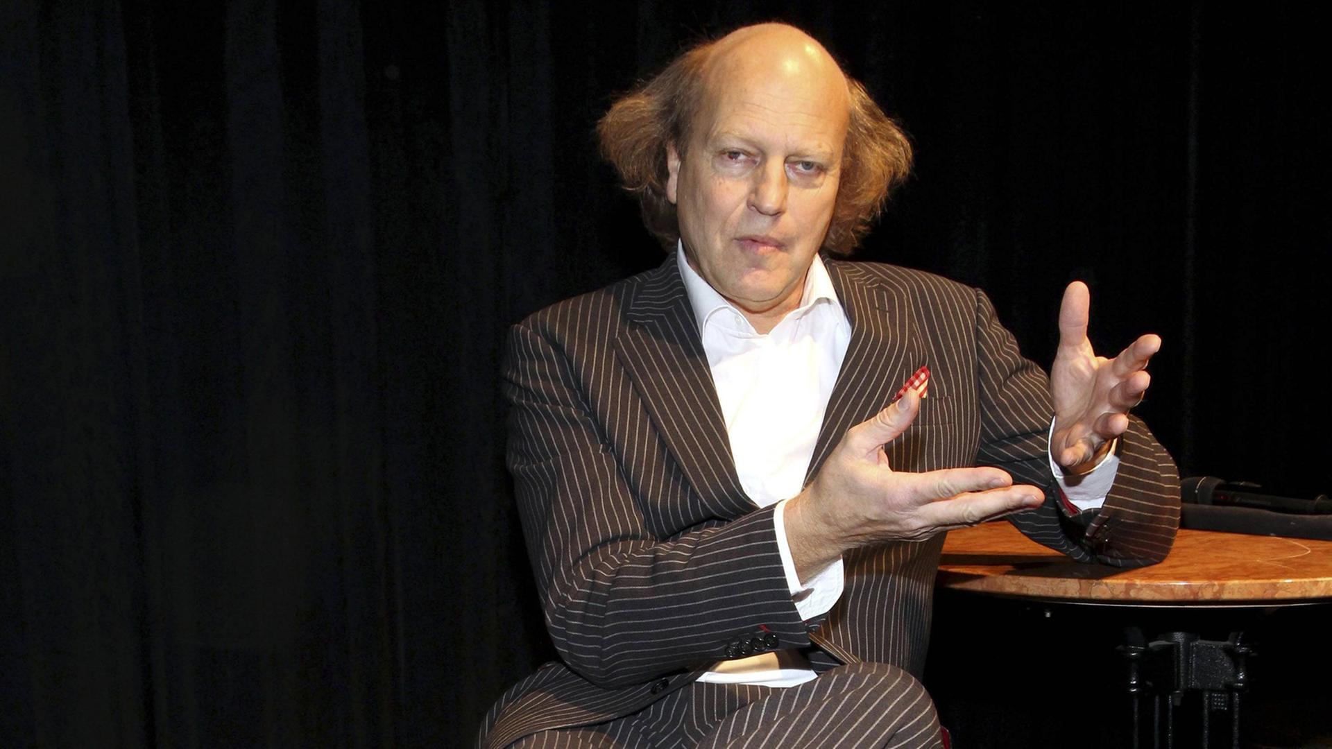 Der Kabarettist, Autor und Schauspieler Arnulf Rating auf einer Bühne sitzend.