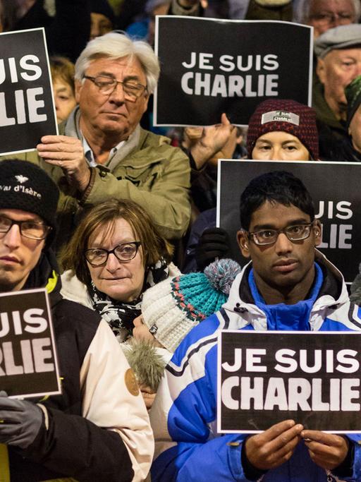 Menschen halten Schilder hoch, auf denen "Je suis Charlie" steht.