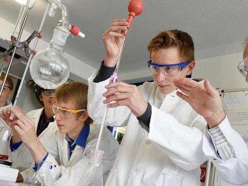 Der Forscher Rudolf Binder (r) beobachtet am 25.09.2015 im Schülerforschungszentrum Südwürttemberg in Bad Saulgau (Baden-Württemberg), wie Schüler Luca Braunger (Mitte) eine bestimmte Menge gefärbtes Wasser mit einer Pipette entnimmt.