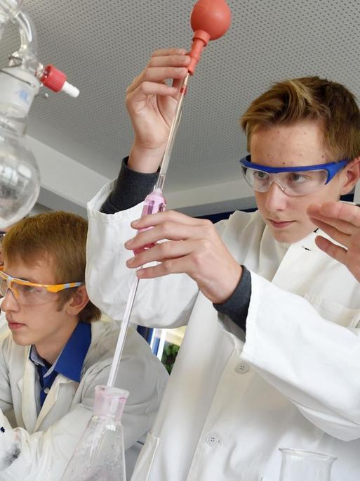 Der Forscher Rudolf Binder (r) beobachtet am 25.09.2015 im Schülerforschungszentrum Südwürttemberg in Bad Saulgau (Baden-Württemberg), wie Schüler Luca Braunger (Mitte) eine bestimmte Menge gefärbtes Wasser mit einer Pipette entnimmt.