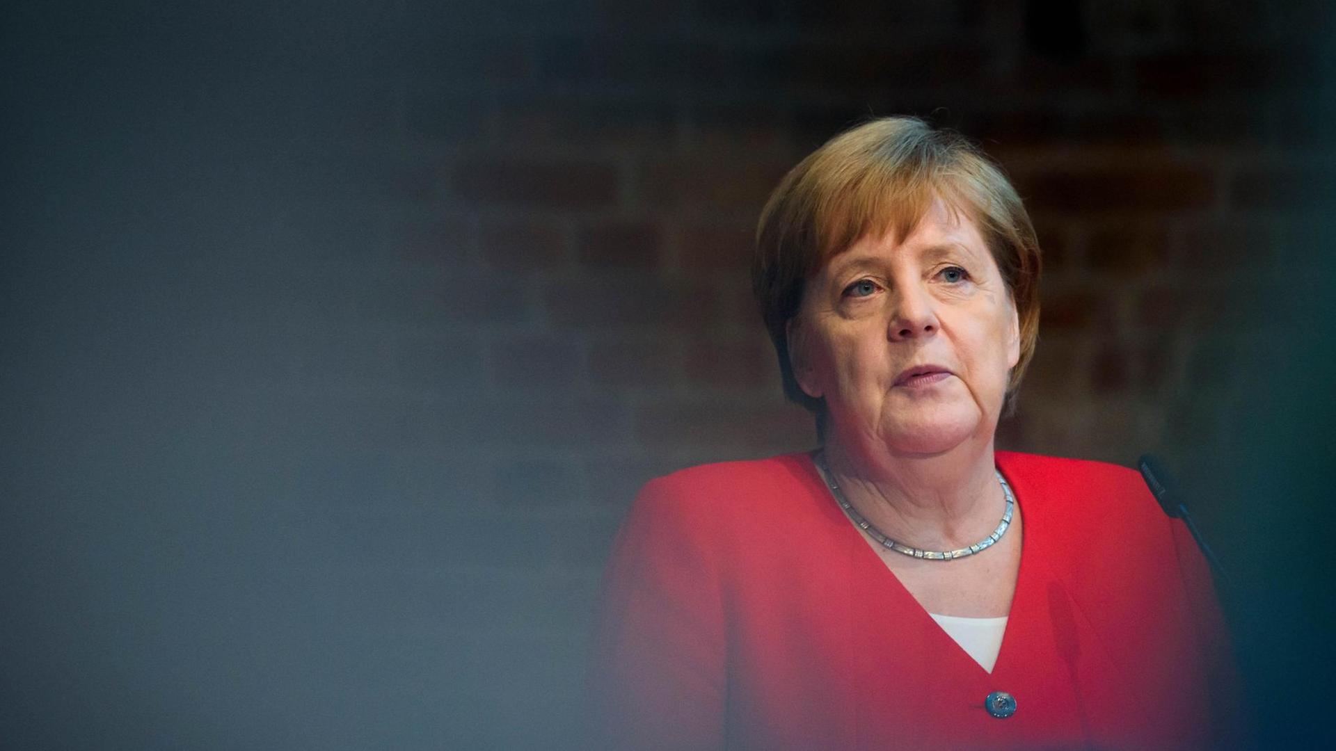 Bundeskanzlerin Angela Merkel (CDU) trägt ein rotes jacket vor dunklem Hintegrund.