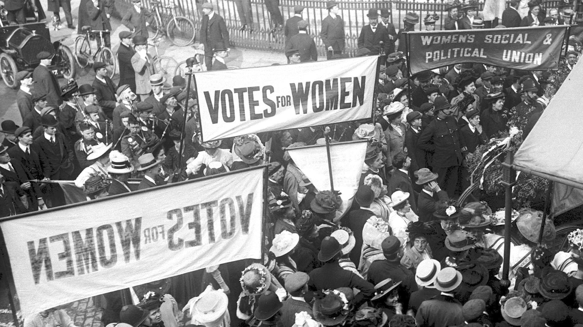 1910 demonstrieren Sufragetten vor den Londoner "Houses of Parliament". Auf ihren Plakaten steht: "Votes for Women", "Womens Social & Political Union".