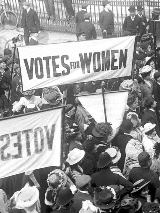 1910 demonstrieren Sufragetten vor den Londoner "Houses of Parliament". Auf ihren Plakaten steht: "Votes for Women", "Womens Social & Political Union".