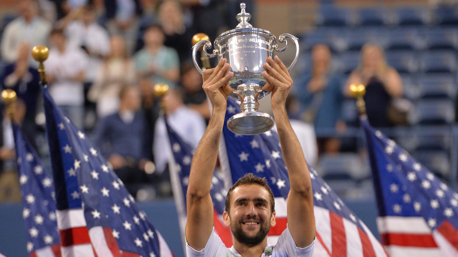 Der kroatische Tennis-Profi Marin Cilic reckt bei den US-Open 2014 den Sieger-Pokal in die Luft. Im Hintergrund sind mehrere US-Flaggen und Publikum zu sehen. Der kroatische Tennis-Profi Marin Cilic reckt bei den US-Open 2014 den Sieger-Pokal in die Luft. Im Hintergrund sind mehrere US-Flaggen und Publikum zu sehen.