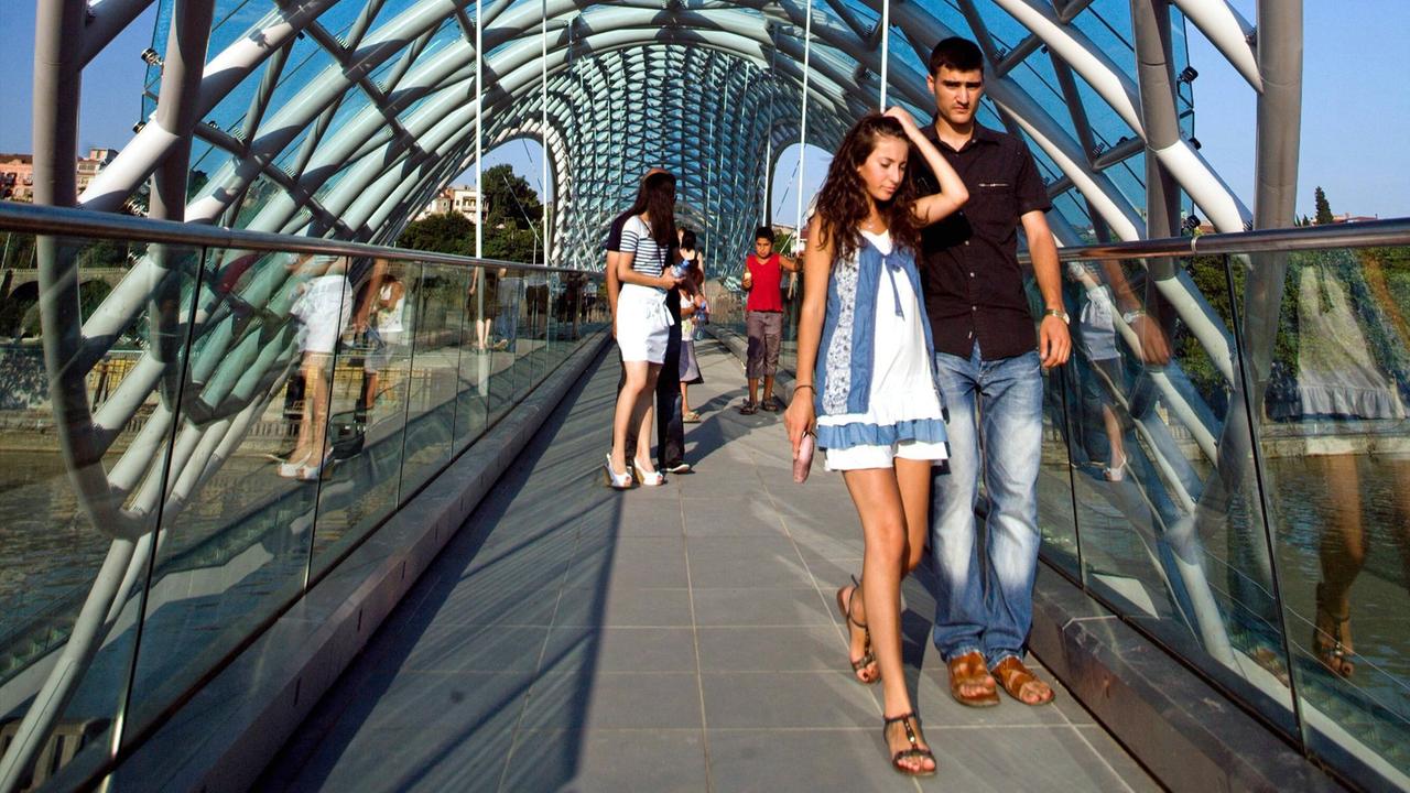 Junge Menschen gehen in Tiflis über die futuristisch gestaltete Friedensbrücke