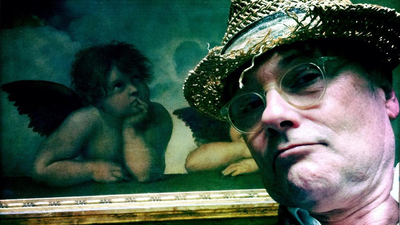 Musikkabarettist Thomas Pigor posiert mit Strohhut vor dem Gemälde "Die Engel der Sixtina" von Raffael