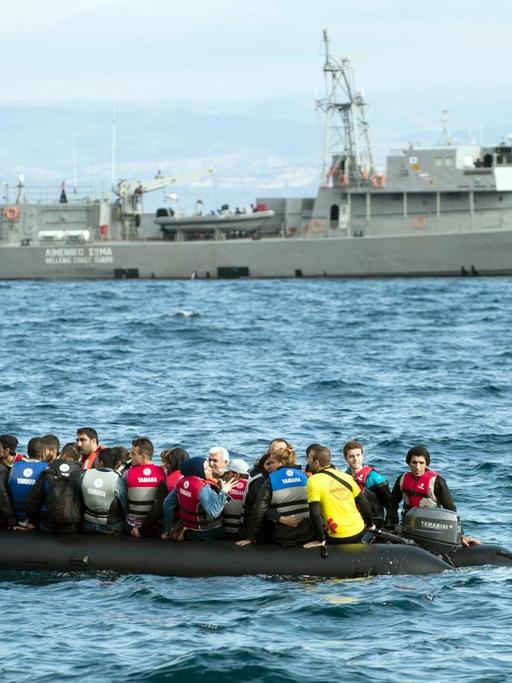 Flüchtlinge fahren am 29.09.2015 mit einem Schlauchboot an einem Schiff der griechischen Küstenwache vorbei.