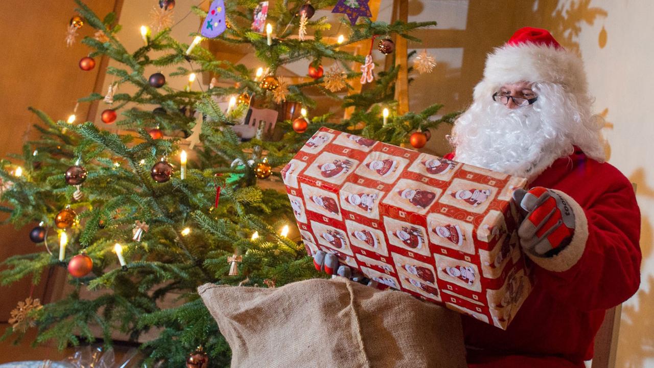 Der Weihnachtsmann sitzt zur Bescherung in einem Haus neben einem geschmückten Weihnachtsbaum