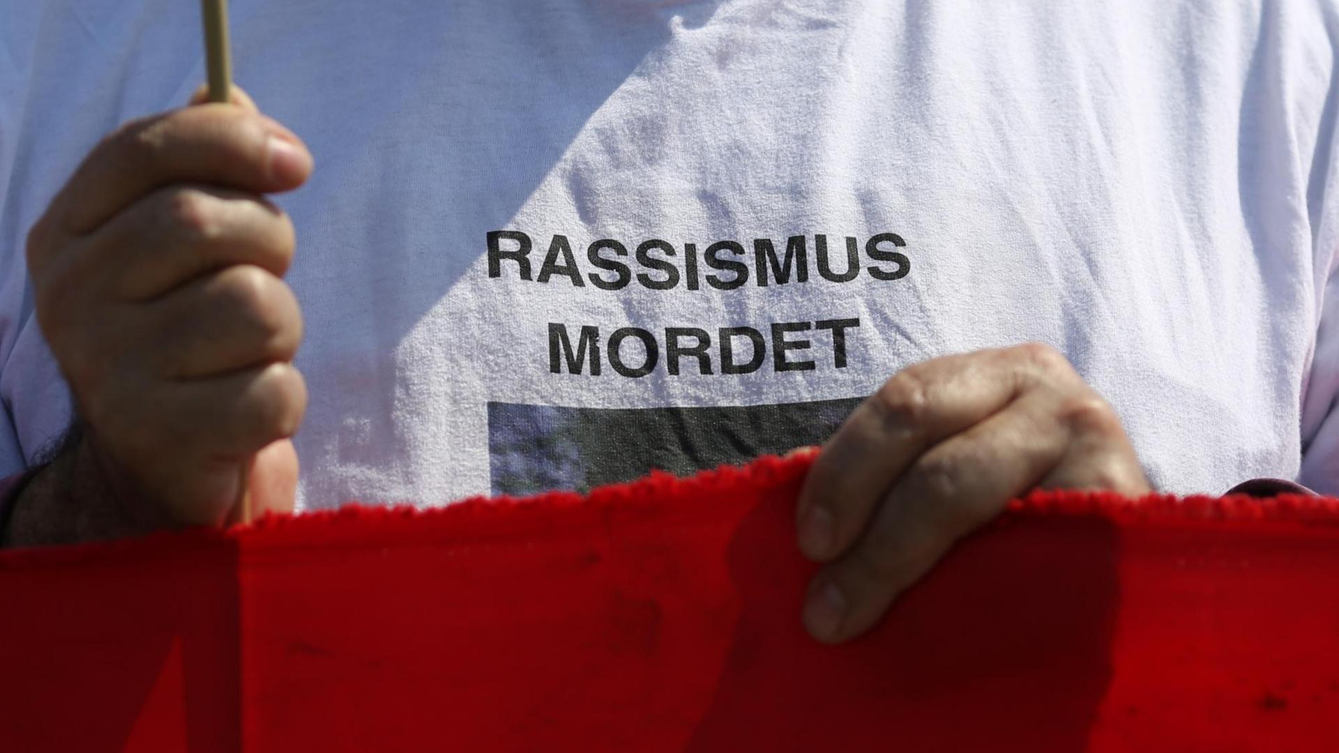 Der Schriftzug "Rassismus mordet" steht auf dem T-Shirt eines Demonstranten vor dem Reichstagsgebäude in Berlin. Mehrere Gruppen hatten am am 06.05.2013 zu einem Gedenken an die Opfer der NSU-Mordserie, als auch für alle anderen Opfer rechter Gewalt aufgerufen.