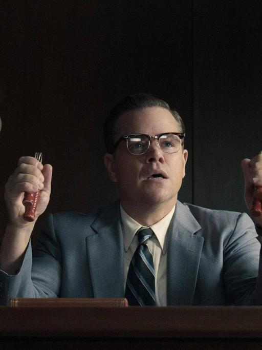 Szenenbild aus Suburbicon: Matt Damon sitzt an einem Schreibtisch und trainiert seine Griffkraft