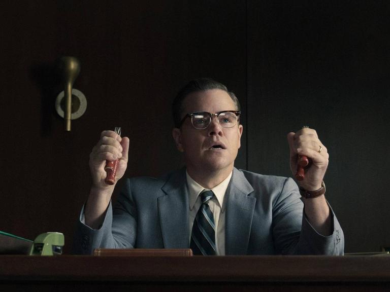 Szenenbild aus Suburbicon: Matt Damon sitzt an einem Schreibtisch und trainiert seine Griffkraft