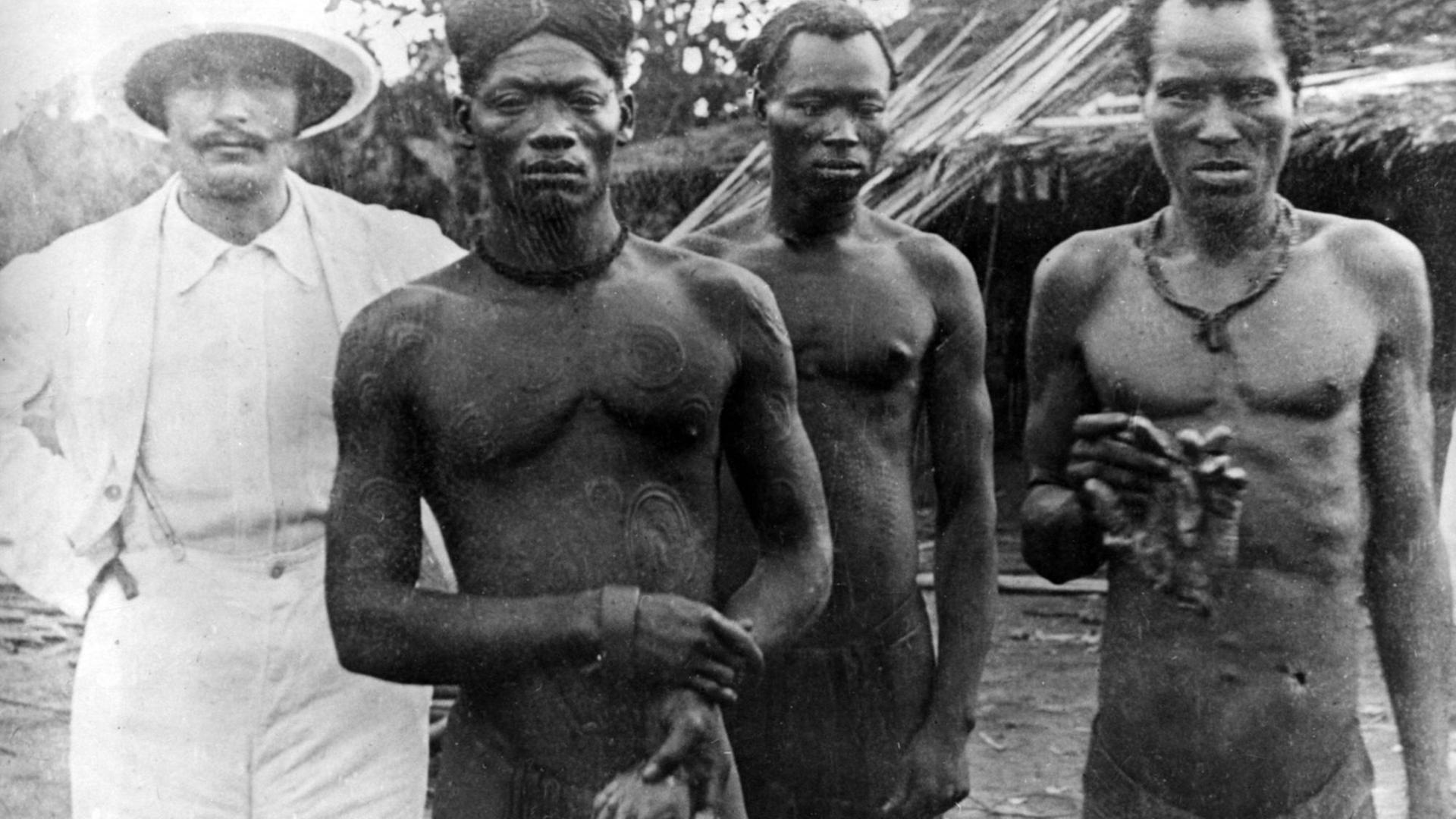 Das Bild ist ungefähr aus dem Jahr 1904. Ein Missionar und zwei kongolesische Männer sind zu sehen.