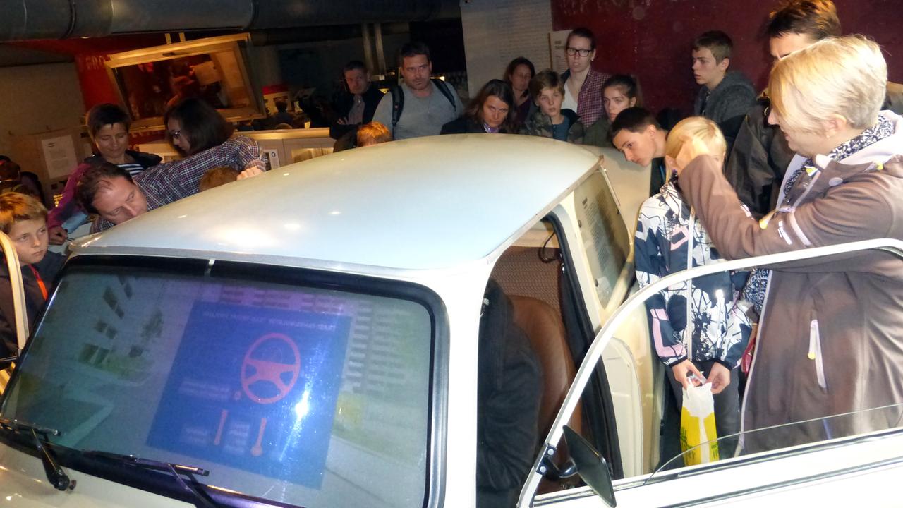 Eine Besuchergruppe umringt neugierig einen Trabant mit Fahrsimulator im DDR-Museum in Berlin.