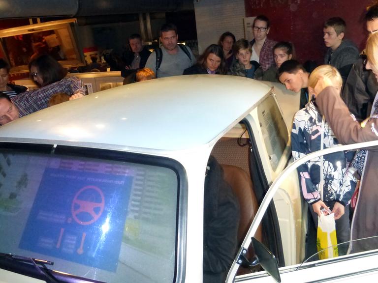 Eine Besuchergruppe umringt neugierig einen Trabant mit Fahrsimulator im DDR-Museum in Berlin. Er erlaubt eine virtuelle Fahrt durch eine Berliner Plattenbausiedlung.