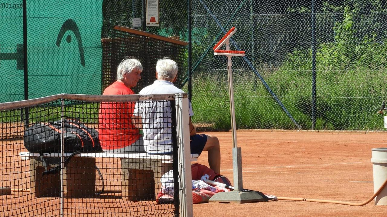 Zwei Tennisspieler ruhen sich auf einer Bank auf dem Tennisplatz aus