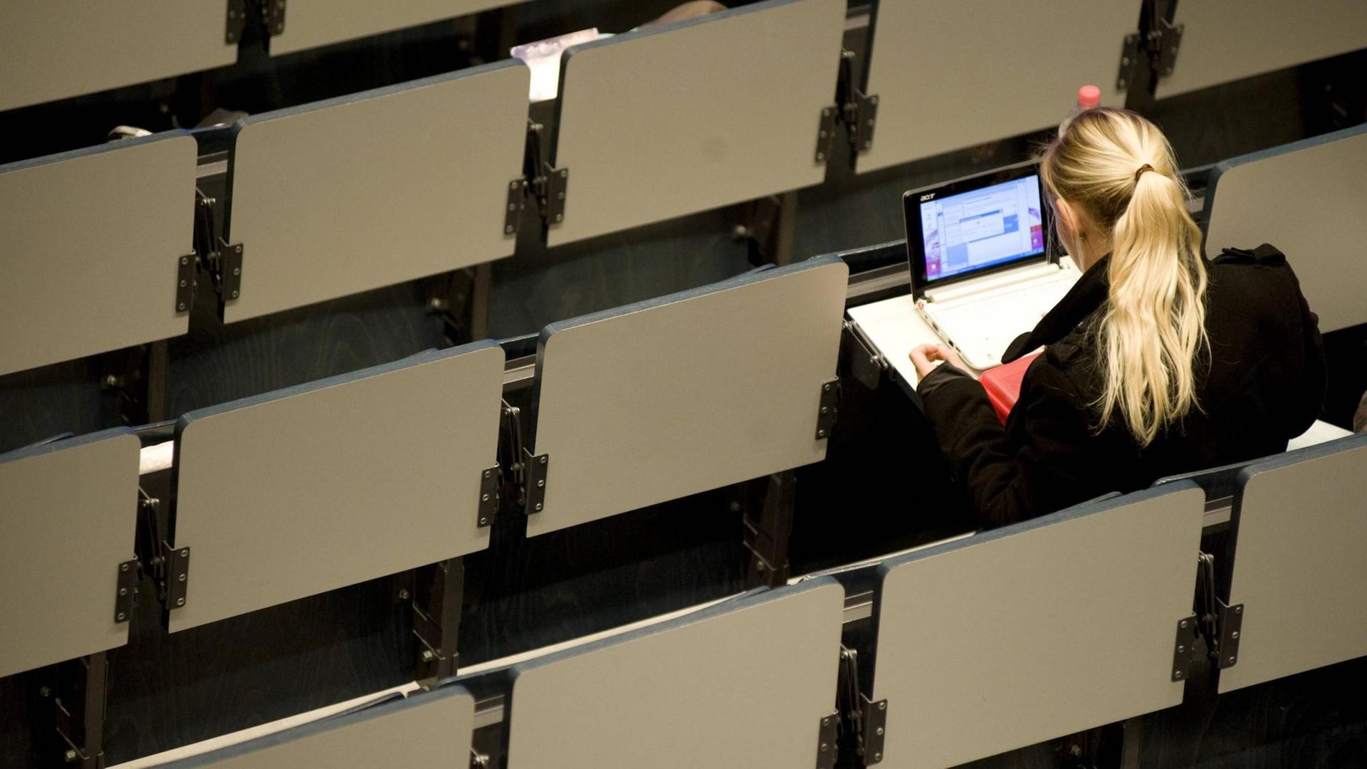 Eine Studentin sitzt allein in einem Hörsaal am Laptop