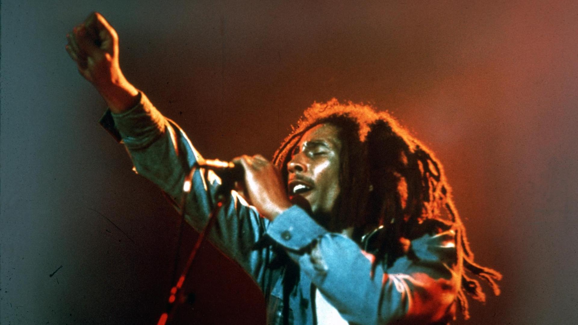 Bob Marley auf der Bühne am Mikrofon, streckt die rechte Faust in die Höhe.