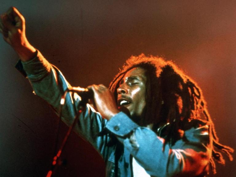 Bob Marley auf der Bühne am Mikrofon, streckt die rechte Faust in die Höhe.