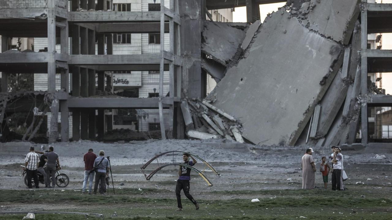 Ein Palästinenser trägt einen Metallrahmen neben einem zerbombten Gebäude.