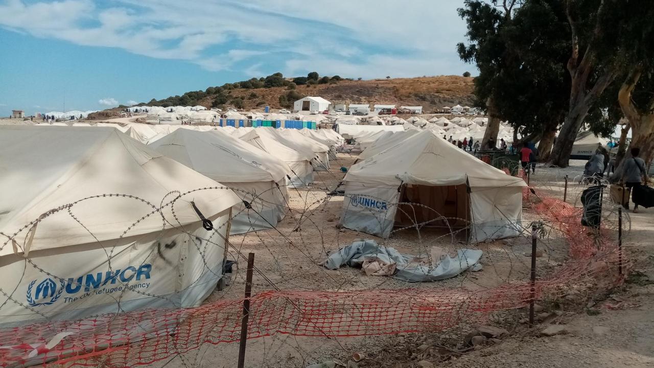 Mehrere weiße spitze Zelte des UNHCR stehen hinter einem Stacheldrahtzaun. Eines ist geöffnet, das Innere ist leer.