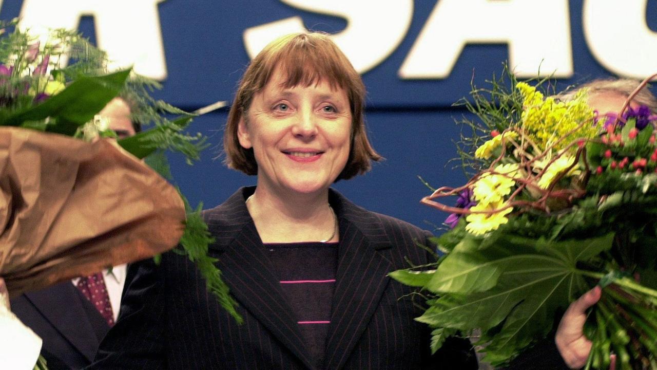 Angela Merkel im Jahr 2000 strahlt mit zwei Blumensträußen in der Hand.